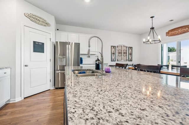 kitchen with white cabinetry, hanging light fixtures, light stone counters, stainless steel fridge, and light wood-type flooring