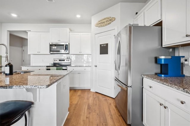 kitchen featuring light stone countertops, light hardwood / wood-style flooring, decorative backsplash, white cabinets, and appliances with stainless steel finishes