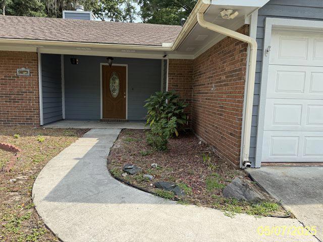 164 W Holly Ave, Kingsland, GA 31548 - doorway to property featuring brick siding, an attached garage, a chimney, and a porch