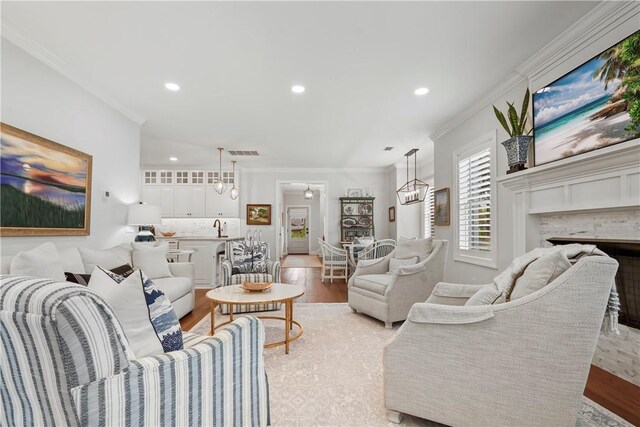 living area featuring visible vents, light wood-style floors, and crown molding