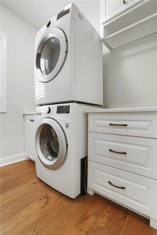 washroom featuring stacked washer / dryer, baseboards, and light wood-type flooring