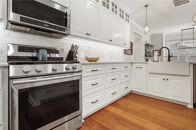 kitchen with visible vents, a sink, appliances with stainless steel finishes, crown molding, and light wood finished floors