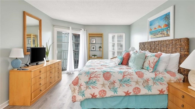 bedroom with access to outside, a textured ceiling, and light wood-type flooring