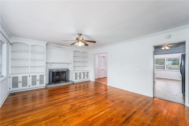 1007 Atlantic Ave, Waycross, GA 31501 - unfurnished living room featuring a ceiling fan, hardwood / wood-style floors, ornamental molding, built in shelves, and a fireplace with raised hearth