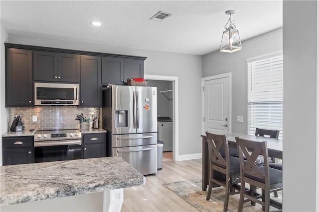 kitchen featuring light wood-type flooring, a textured ceiling, appliances with stainless steel finishes, decorative light fixtures, and light stone counters