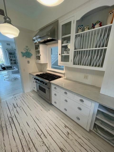 kitchen with glass insert cabinets, wall chimney range hood, light countertops, stainless steel range, and white cabinetry