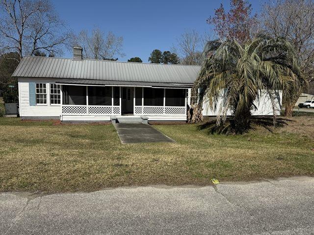 ranch-style home with a front yard, a chimney, a sunroom, and metal roof