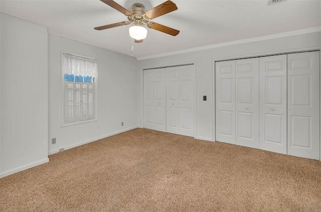 unfurnished bedroom with carpet, a textured ceiling, ceiling fan, and multiple closets