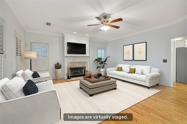 living room featuring a textured ceiling, ceiling fan, light wood-type flooring, and crown molding