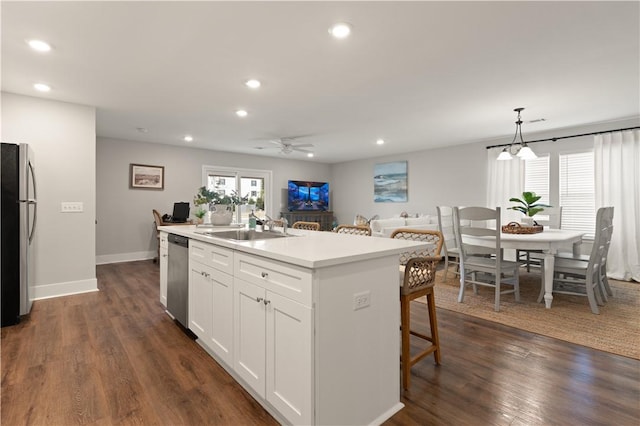 kitchen with white cabinetry, dark wood-type flooring, stainless steel appliances, decorative light fixtures, and a kitchen island with sink