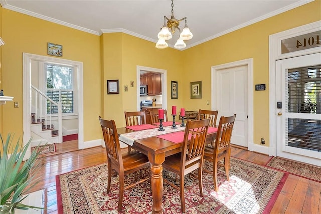 dining space featuring light wood finished floors, a notable chandelier, crown molding, and baseboards