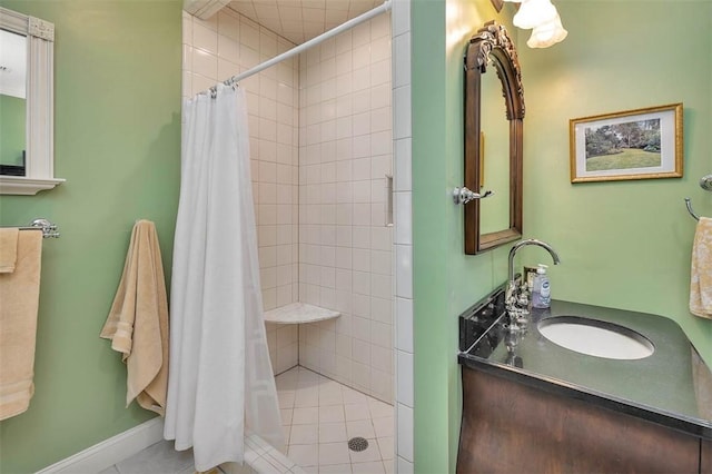 bathroom with tiled shower, vanity, and baseboards