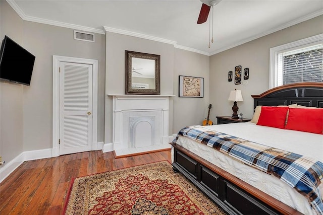 bedroom with visible vents, ornamental molding, hardwood / wood-style flooring, a fireplace, and baseboards