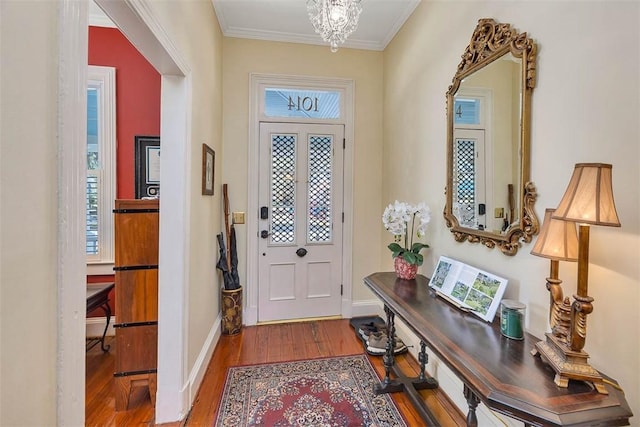 foyer entrance with a chandelier, crown molding, baseboards, and wood finished floors