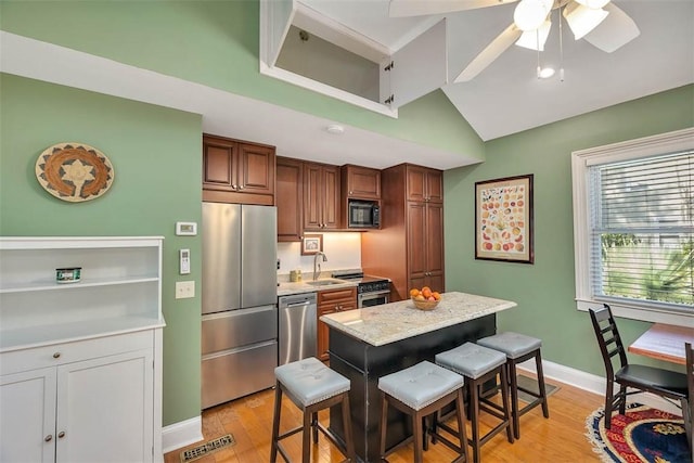 kitchen featuring visible vents, light wood-style flooring, stainless steel appliances, a breakfast bar area, and lofted ceiling