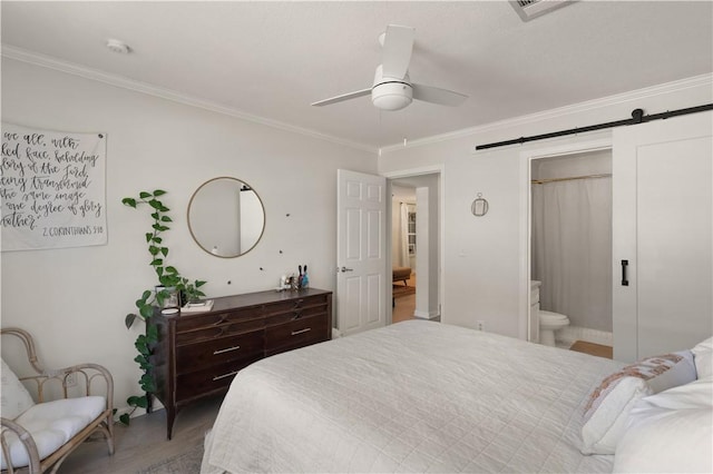 bedroom featuring crown molding, ensuite bath, ceiling fan, a barn door, and wood-type flooring