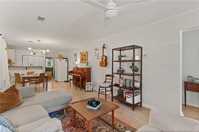 living room with ceiling fan with notable chandelier, ornamental molding, and light hardwood / wood-style flooring