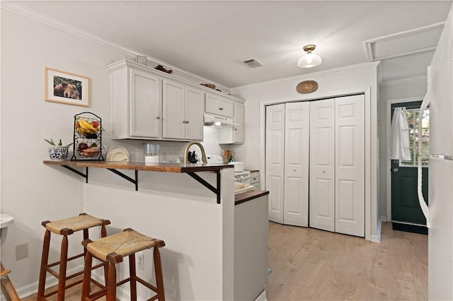 kitchen featuring white cabinets, light hardwood / wood-style flooring, ornamental molding, a kitchen bar, and kitchen peninsula