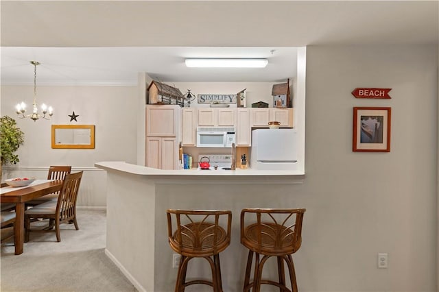 kitchen with a kitchen bar, white appliances, light colored carpet, pendant lighting, and a notable chandelier