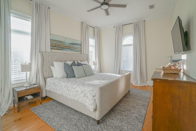 bedroom featuring multiple windows, ceiling fan, ornamental molding, and light wood-type flooring