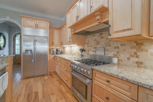 kitchen featuring high end appliances, light stone counters, premium range hood, light brown cabinetry, and light wood-type flooring