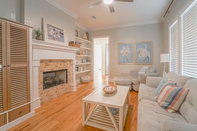 living room with ceiling fan, light wood-type flooring, a fireplace, ornamental molding, and built in features