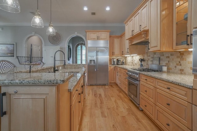 kitchen with hanging light fixtures, ornamental molding, high quality appliances, light brown cabinetry, and light wood-type flooring