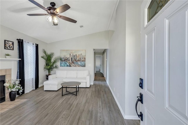 living room with a tile fireplace, ceiling fan, light hardwood / wood-style flooring, and vaulted ceiling