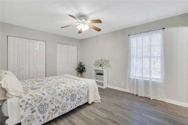 bedroom featuring hardwood / wood-style floors, a textured ceiling, ceiling fan, and multiple closets