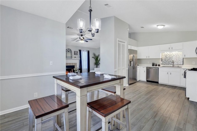 kitchen with white cabinets, appliances with stainless steel finishes, decorative light fixtures, wood-type flooring, and a tiled fireplace