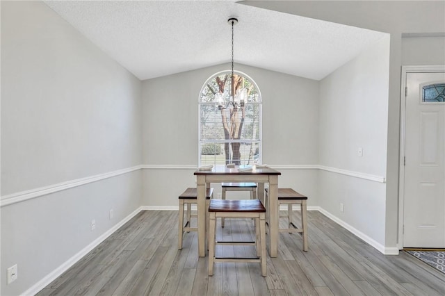 dining space with hardwood / wood-style floors, an inviting chandelier, a textured ceiling, and vaulted ceiling