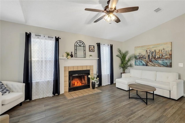 living room with wood-type flooring, lofted ceiling, and a tiled fireplace