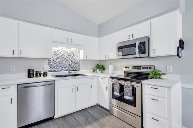 kitchen featuring stainless steel appliances, sink, hardwood / wood-style flooring, white cabinetry, and lofted ceiling