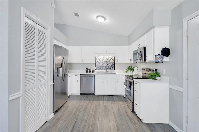 kitchen featuring lofted ceiling, white cabinets, sink, light hardwood / wood-style floors, and stainless steel appliances