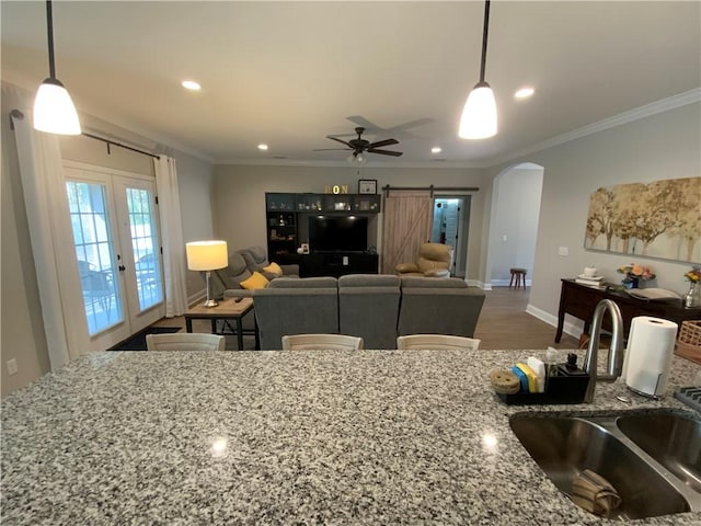 kitchen with light stone counters, sink, crown molding, and decorative light fixtures