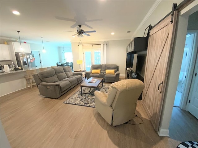 living room with ornamental molding, light hardwood / wood-style floors, a barn door, and ceiling fan