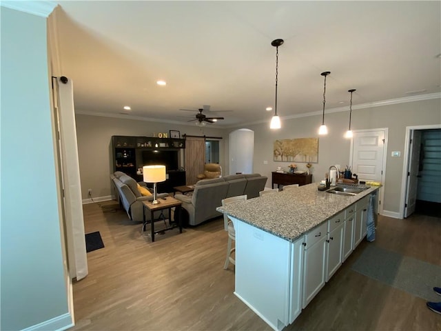 kitchen with a breakfast bar, sink, white cabinets, light stone counters, and a center island with sink