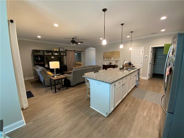 kitchen featuring decorative light fixtures, an island with sink, white cabinets, light stone counters, and stainless steel appliances