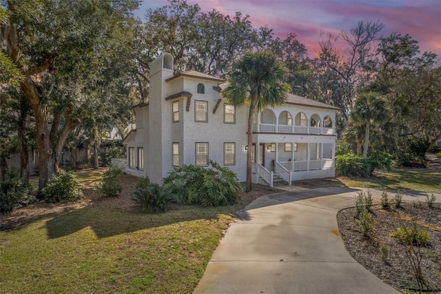 mediterranean / spanish-style house featuring a porch, a balcony, driveway, stucco siding, and a front lawn