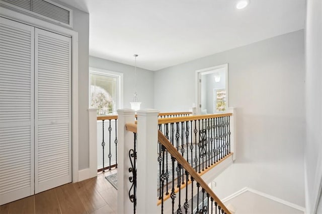 hall featuring baseboards, visible vents, wood finished floors, and an upstairs landing