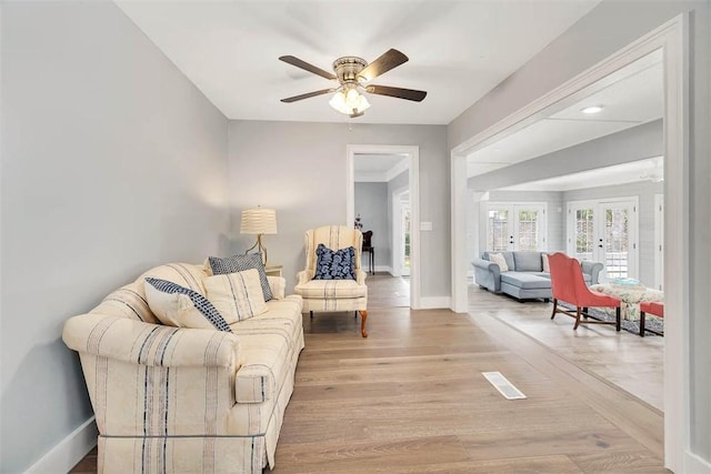 living room with light wood-type flooring, baseboards, a ceiling fan, and french doors