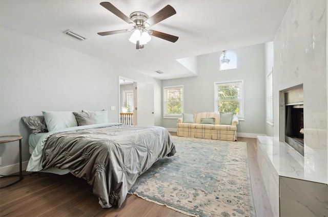 bedroom featuring wood finished floors, a ceiling fan, baseboards, visible vents, and a high end fireplace