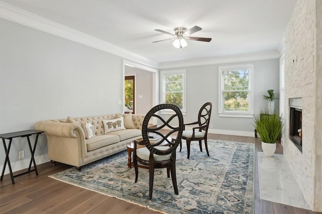 living area with ornamental molding, a fireplace, baseboards, and wood finished floors