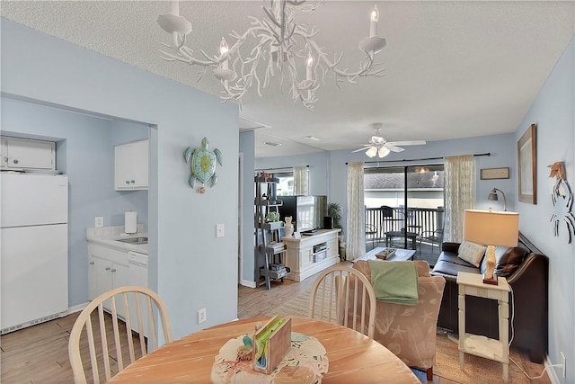 dining area featuring ceiling fan with notable chandelier, light hardwood / wood-style floors, sink, and a textured ceiling