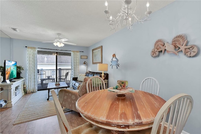 dining space featuring ceiling fan with notable chandelier, a textured ceiling, and light hardwood / wood-style flooring