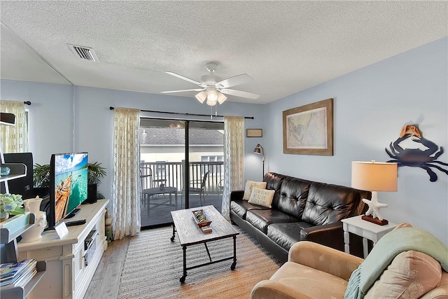 living room featuring ceiling fan, a textured ceiling, and light wood-type flooring