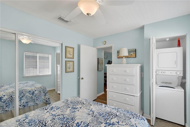 bedroom with stacked washer / dryer, ceiling fan, a textured ceiling, and hardwood / wood-style flooring