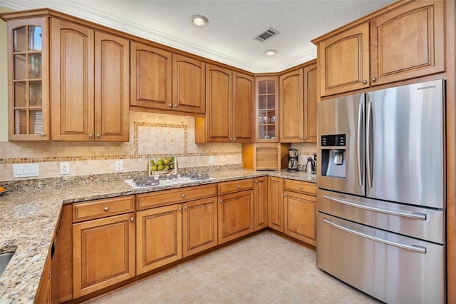 kitchen with stainless steel refrigerator with ice dispenser, brown cabinetry, visible vents, and light stone countertops