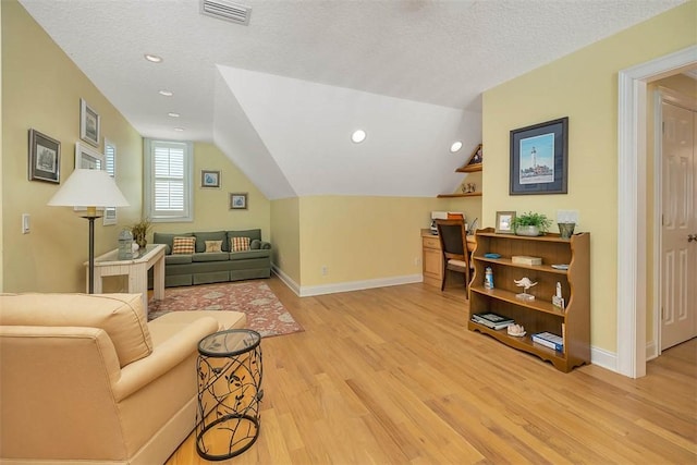 interior space featuring a textured ceiling, visible vents, vaulted ceiling, baseboards, and light wood-style flooring