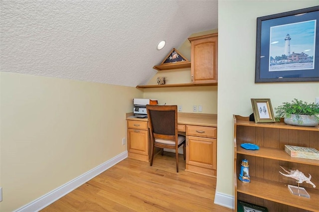 office area with built in study area, light wood-style floors, a textured ceiling, baseboards, and vaulted ceiling